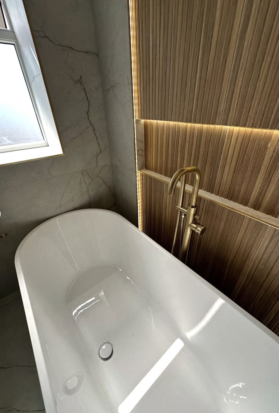 Freestanding bath with brass floorstanding tap against a lit fluted wall