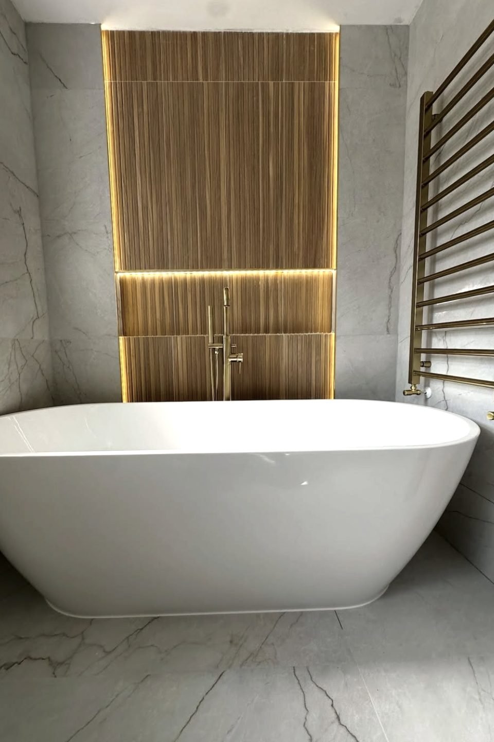 Freestanding bath in front of a lit fluted feature wall with brass towel rail
