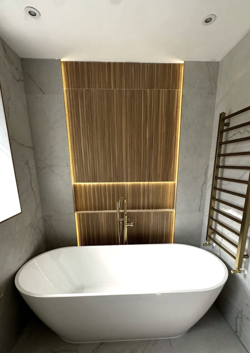 Freestanding bath set into a marble alcove with a lit fluted feature wall