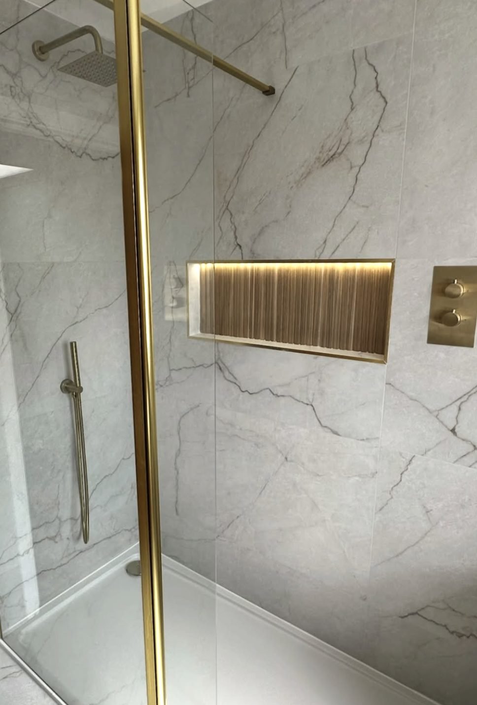 Walk-in shower with gold framed screen, marble walls and a lit fluted niche