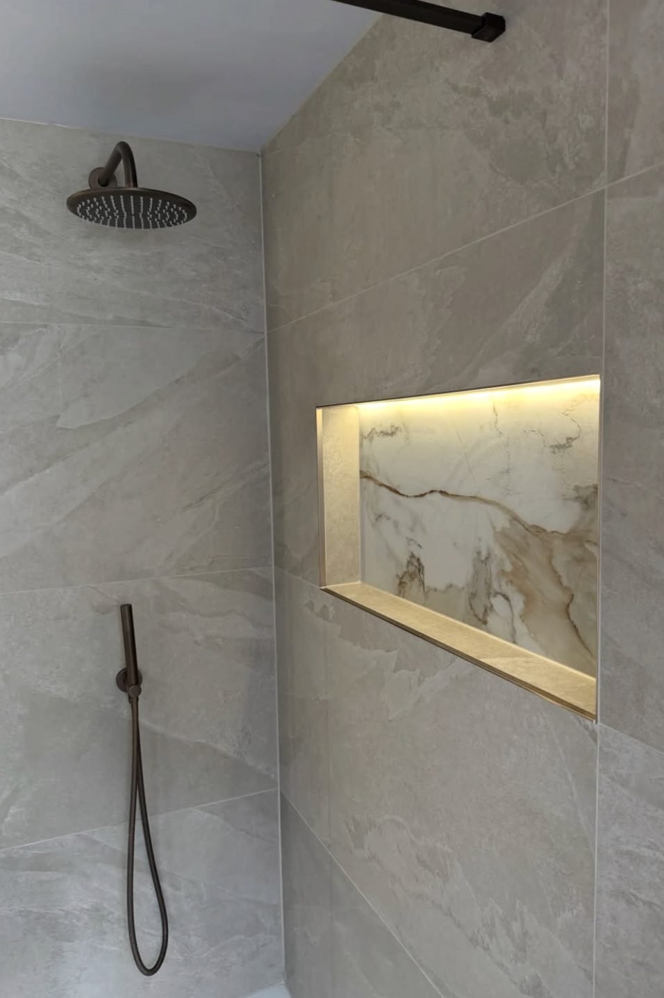 Lit marble recess inside a stone effect shower with brass fittings