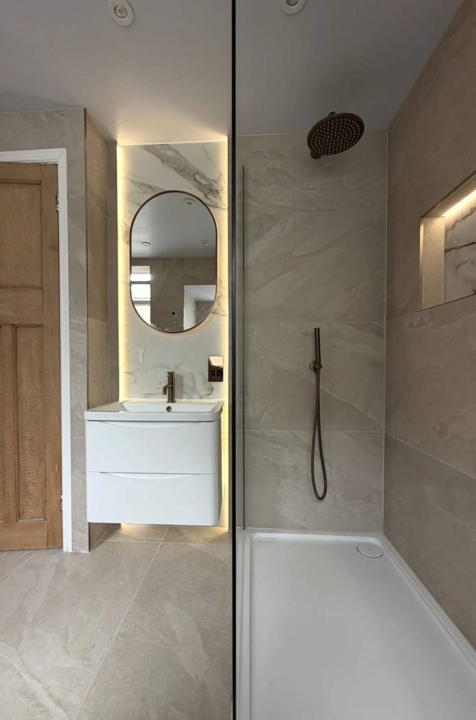 Compact stone effect en-suite with wall hung vanity and lit oval mirror
